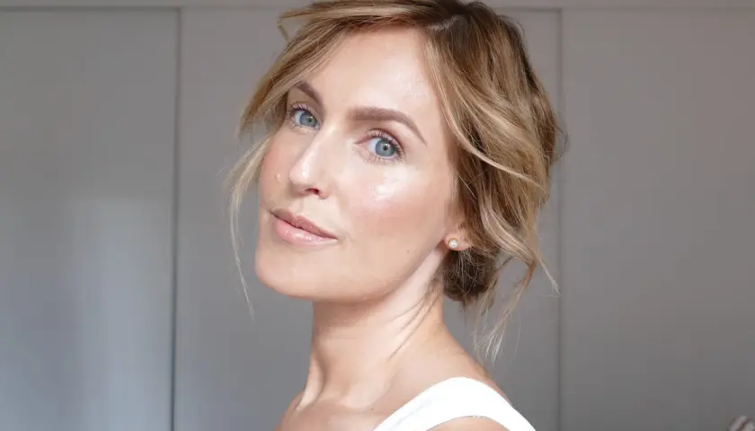 En kvinna med blå ögon och blont hår som har fått en fin lyster efter att ha applicerat highlighter.
