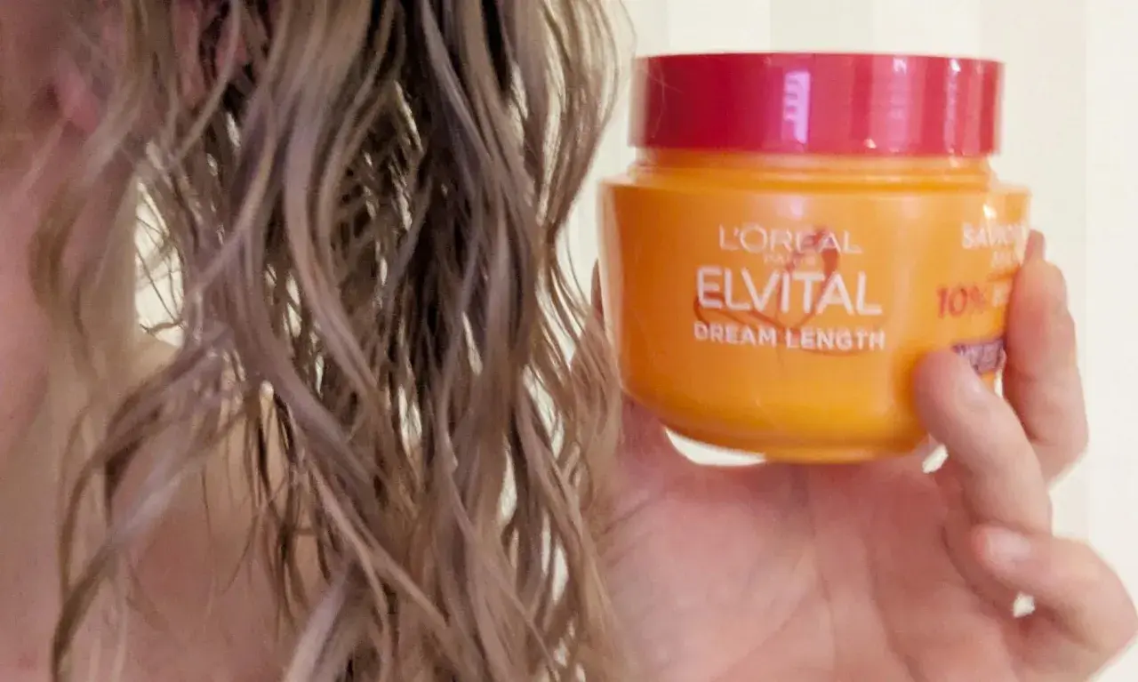En hand håller en burk med L'Oréal Elvital Dream Length hårinpackning bredvid blekt, vått hår.
