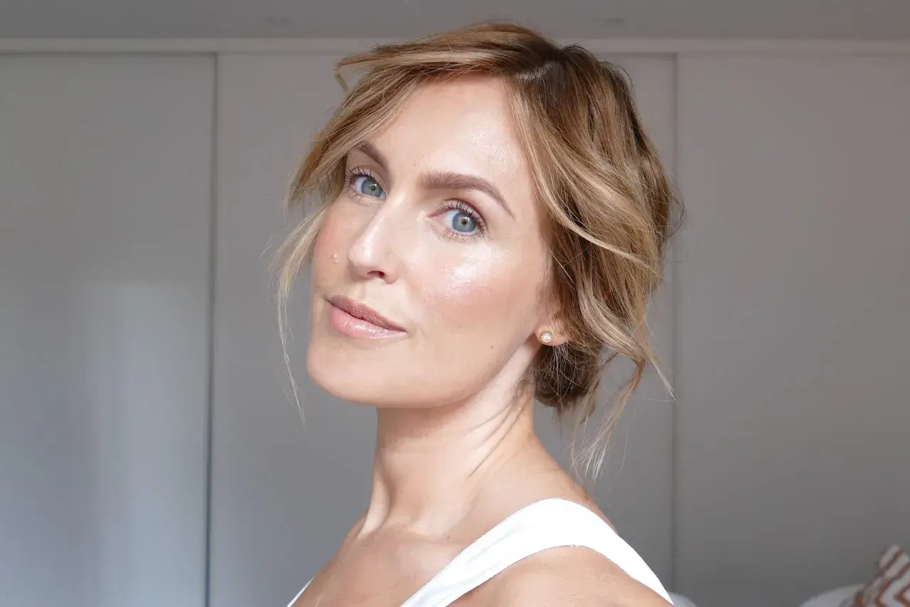 En kvinna med blå ögon och blont hår som har fått en fin lyster efter att ha applicerat highlighter.