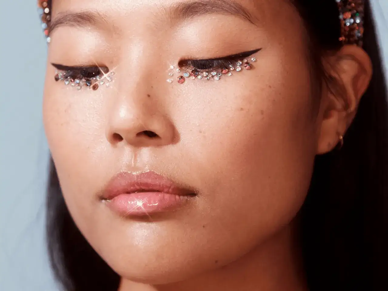 En n&auml;rbild p&aring; en ung kvinna med glittrande &ouml;gonlock och en skarp eyeliner. Hon har en glansig l&auml;ppglans och en gnistrande tiara.