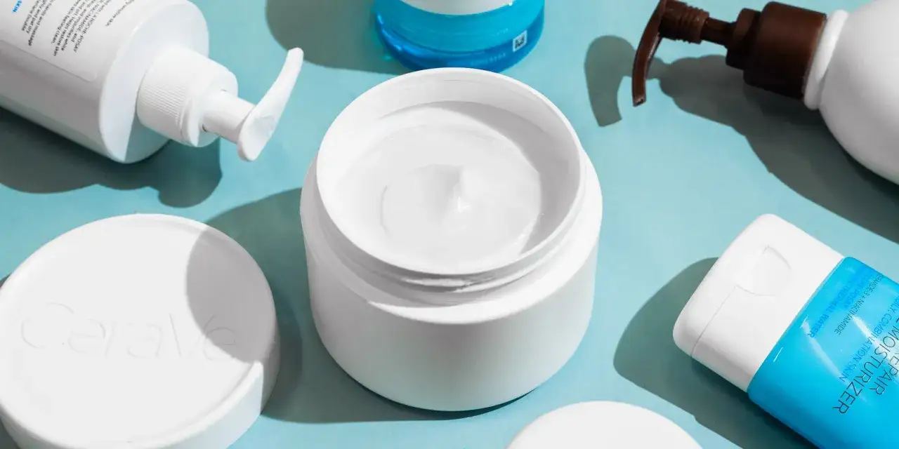 En &ouml;ppen burk med vit body lotion i ansiktet, omgiven av andra hudv&aring;rdsprodukter.
